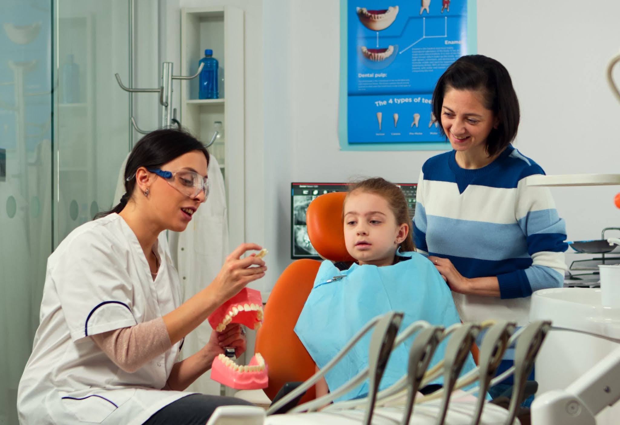 Dentist teaching a young patient about oral health while her mother watches during a family dental visit.